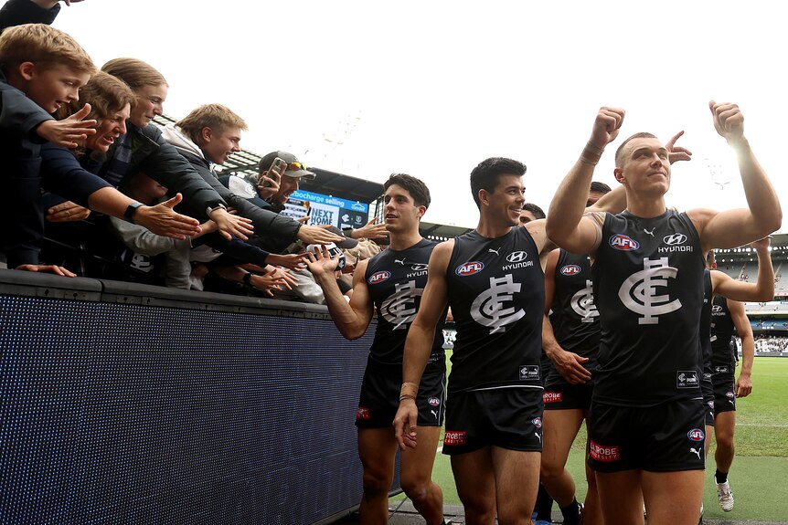 An AFL captain walks down the race with his team, giving a thumbs up to the crowd after a win.  