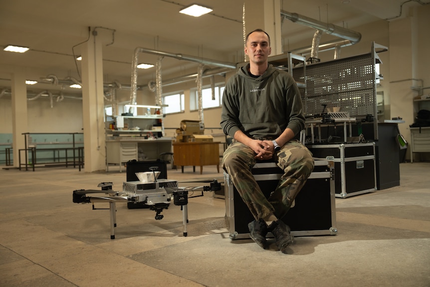 Man sitting on a black box with a drone next to him on the ground.