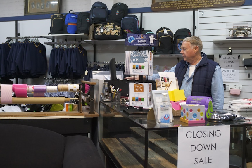 A man in a blue vest stands behind a shop counter typing into a computer 