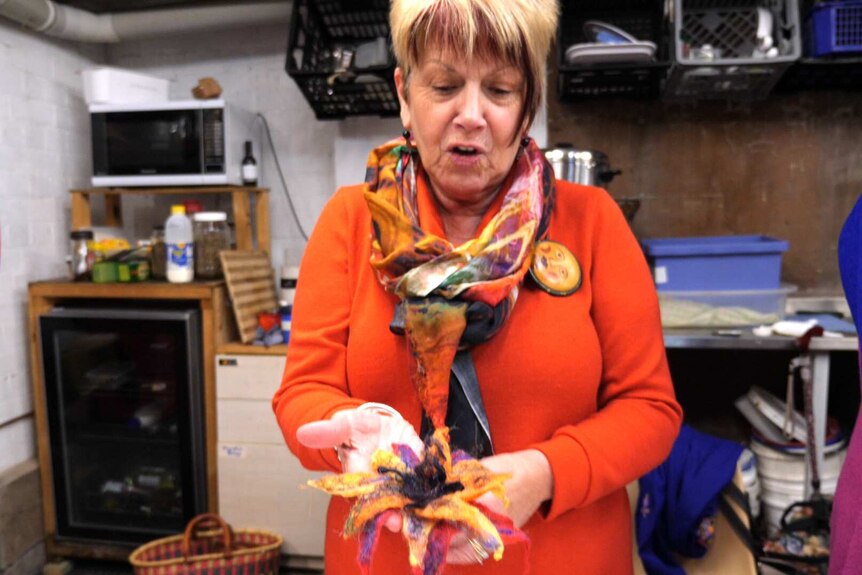 A woman in an orange cardigan holds a completed felt flower.