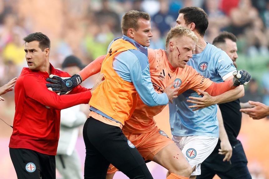 An injured man wearing an orange soccer uniform is assisted by others.