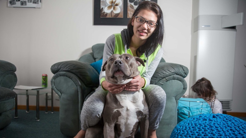 Christine sits on couch chair with her dog, her daughter sits on the ground beside her