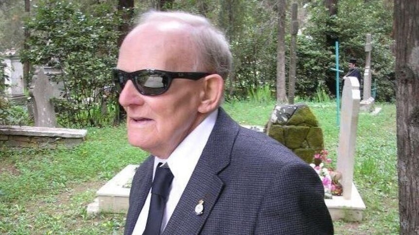 An elderly man with sunglasses and war badges on his suit jacket shot in a graveyard
