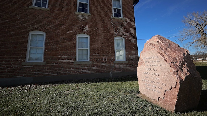 stone outside the genoa indian school, an old brick building, in memory of the unknown native american children that died there