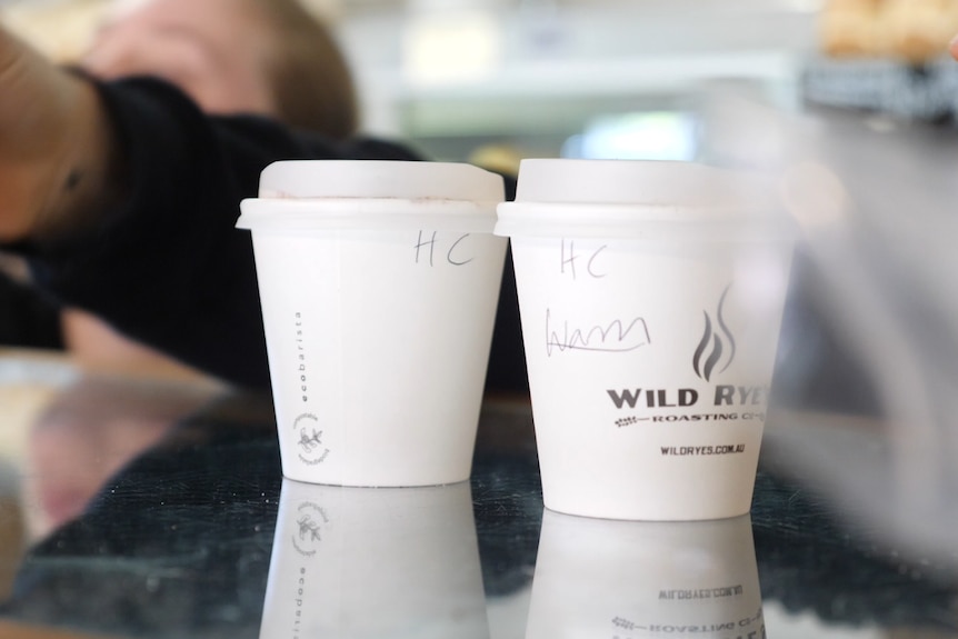 Two white coffee cups with shorthand for 'hot chocolate' written on them