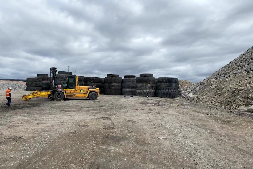 A pile of large tyres on a dirt road with a man operating heavy machinery.