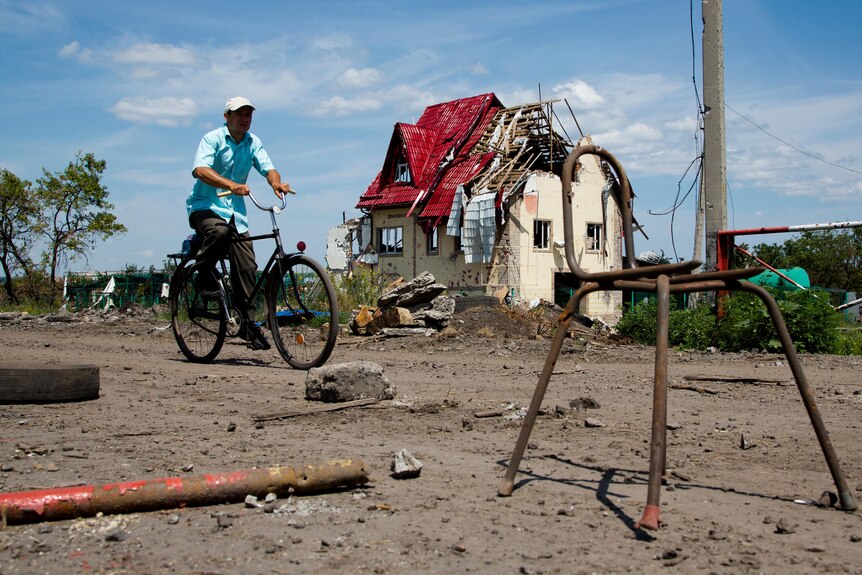  A man rides a bike past a house damaged during fighting.