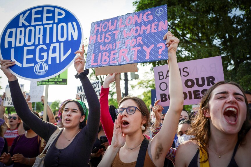 Young female protesters holding signs reading "Keep abortion Legal" and "How long must women wait for liberty"