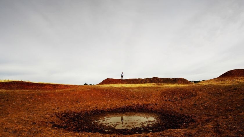 A farmer inspects a dried up dam on his farm.