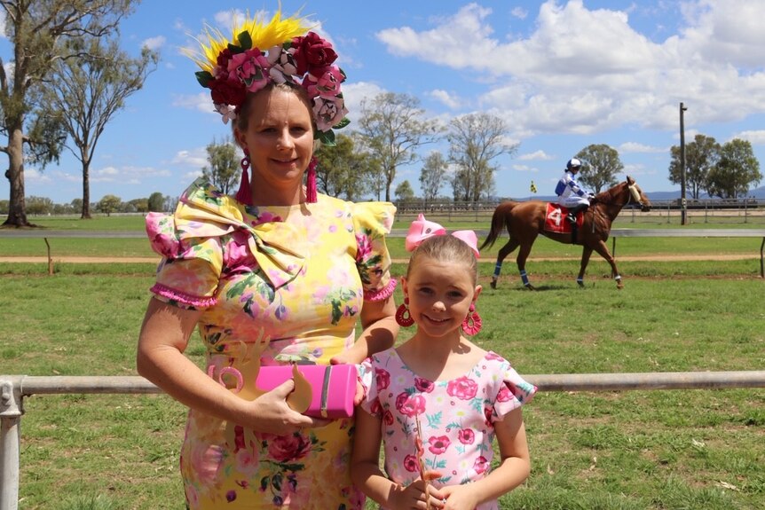 A woman in a flowery hat with her young daughter with a horse in the background