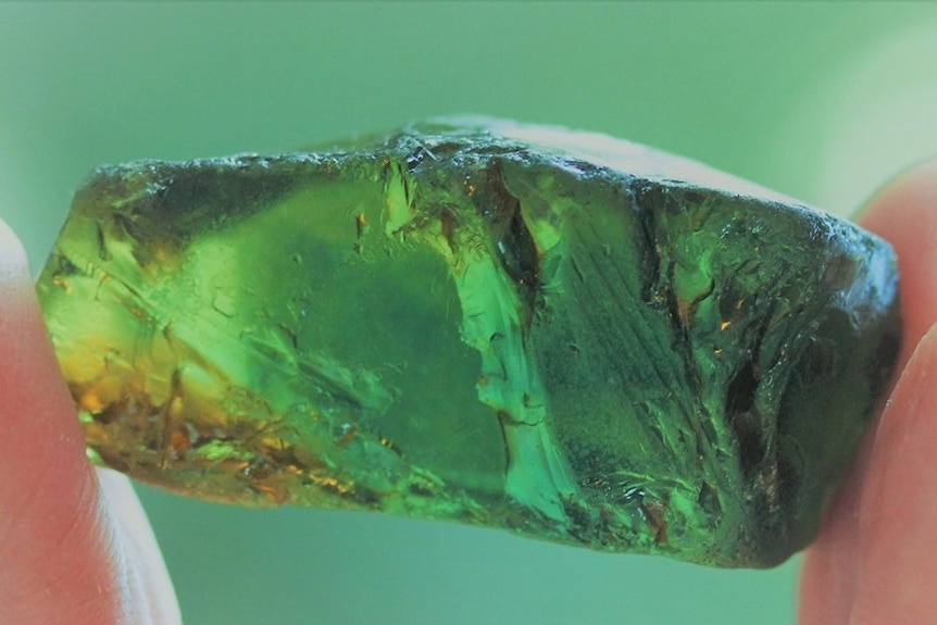 A large green gem stone is held between two fingers.