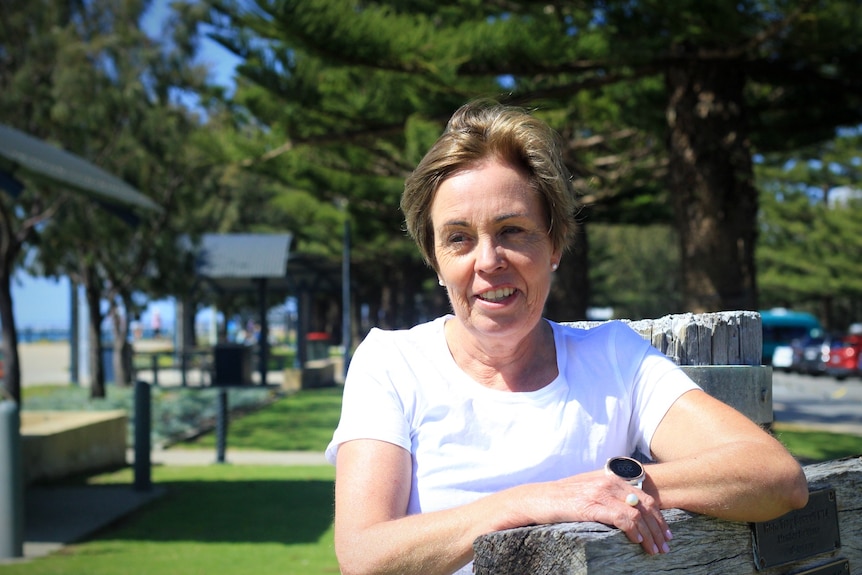 A smiling, middle-aged woman with short hair sitting at a bench in a park.