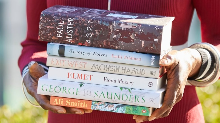 Colour photograph of a person in a red top holding a stack of the Man Book Prize 2017 shortlisted books.