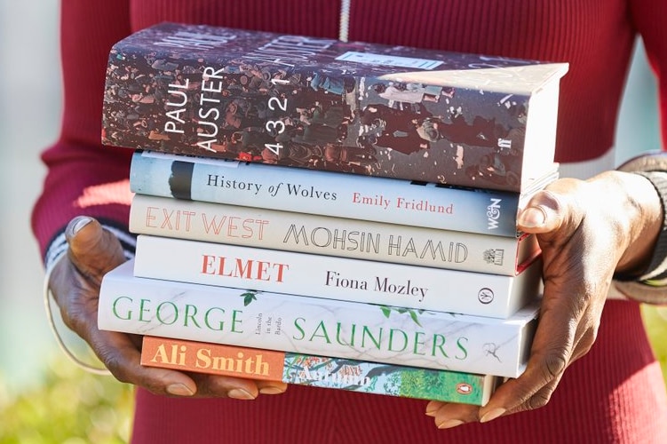 Colour photograph of a person in a red top holding a stack of the Man Book Prize 2017 shortlisted books.