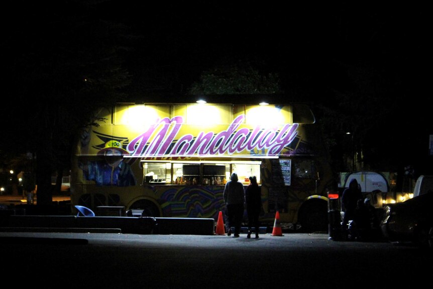 The Mandalay Bus Food Van illuminated by lights at night.