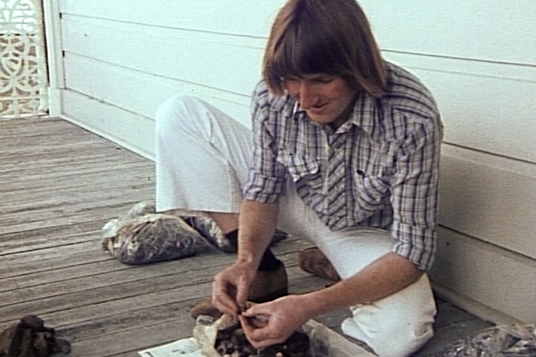 A man sitting on the ground looking through fragments of bone and other archaeological finds.
