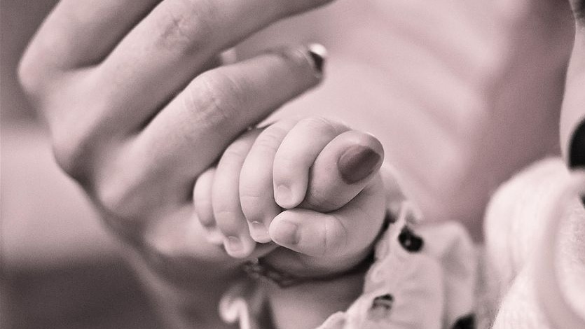 Sepia coloured photo of a small baby's hand holding a mother's finger