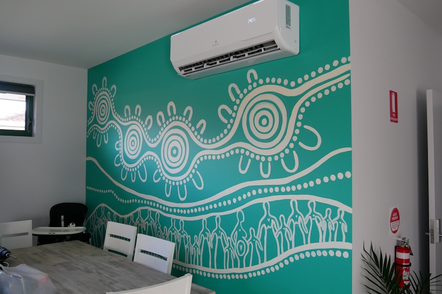 A large aqua wall in the dining room has a large line and dot Aboriginal artwork. 