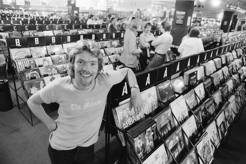 Black-and-white archival image of Richard Branson in his record store in London, standing in front of a row of records.
