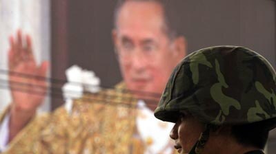 Thai soldier stands guard in front of a building draped with a portrait of Thai King Bhumibol