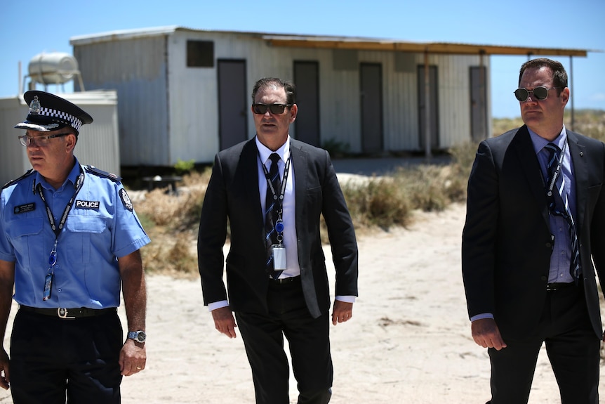 Three police officers - two in suits- walking at a campsite with their sunglasses on