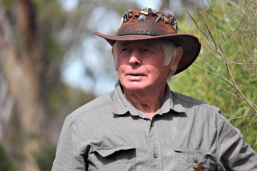 He wears an akubra covered in brooches and has white hair