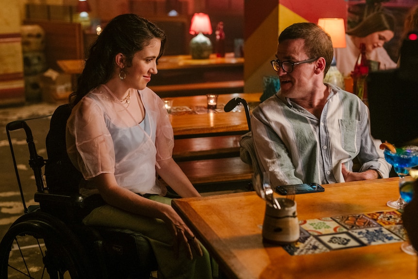 A young women in a wheelchair is talking to a young man in a wheelchair in a bar somewhere.