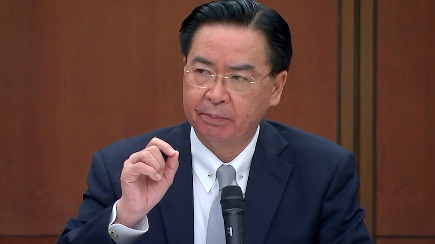 A Taiwanese wearing a suit man gestures while holding a microphone.