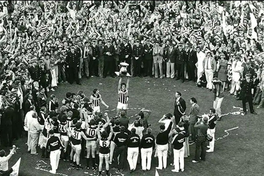 Black and white photograph of Russell Ebert holding trophy surrounded by hundreds of people.