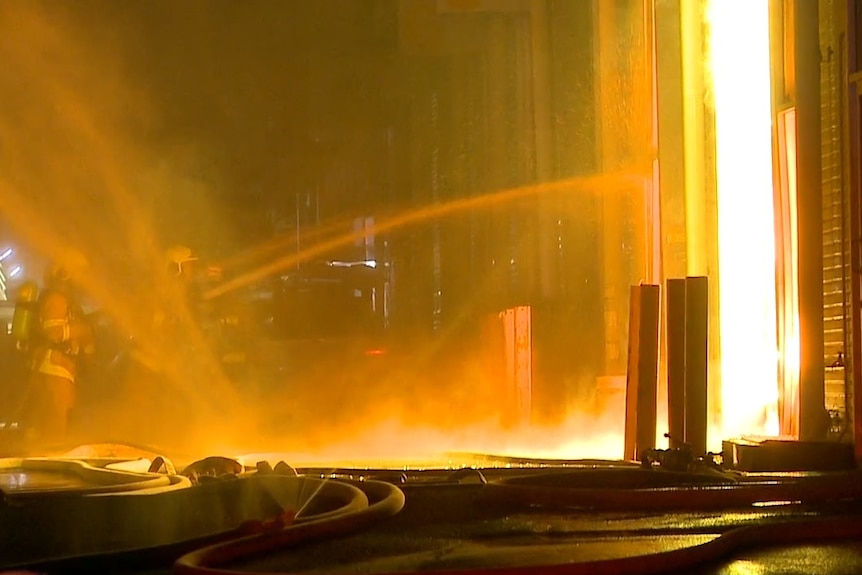 firefighters hosing a burning warehouse doorway