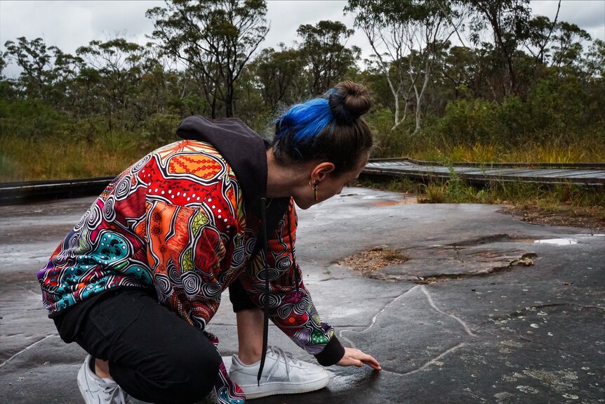 A woman looking at an ancient Aboriginal rock carving.