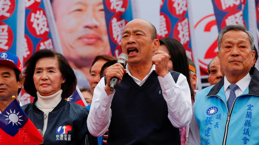 Han Kuo-yu speaks into a microphone while supporters stand behind him.