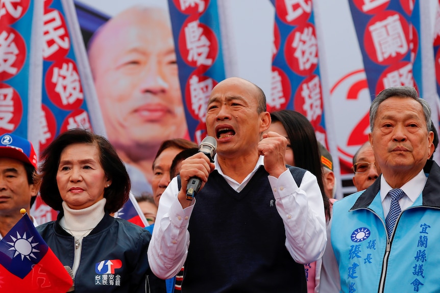 Han Kuo-yu speaks into a microphone while supporters stand behind him.