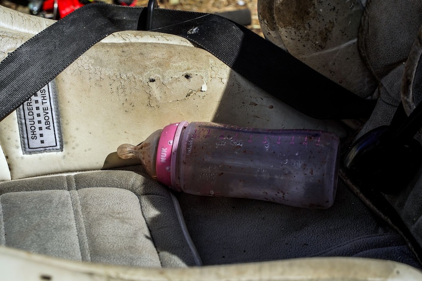 A baby bottle on a weathered car seat.