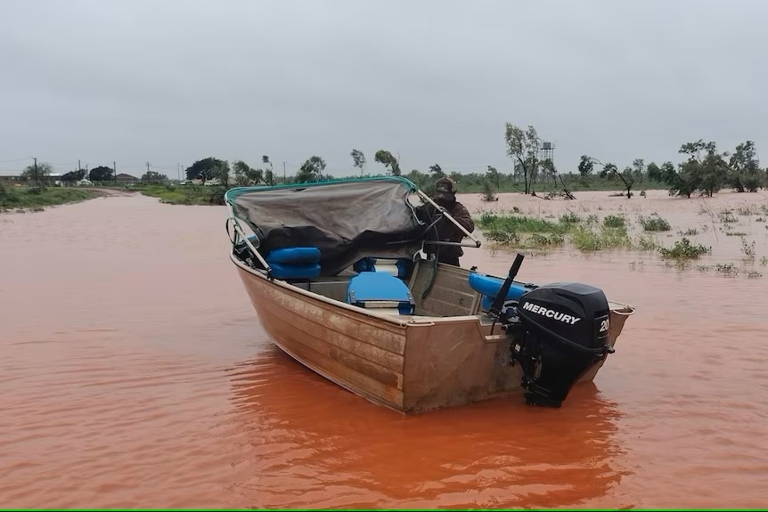 A small tinny boat on a huge brown expanse of floodwaters
