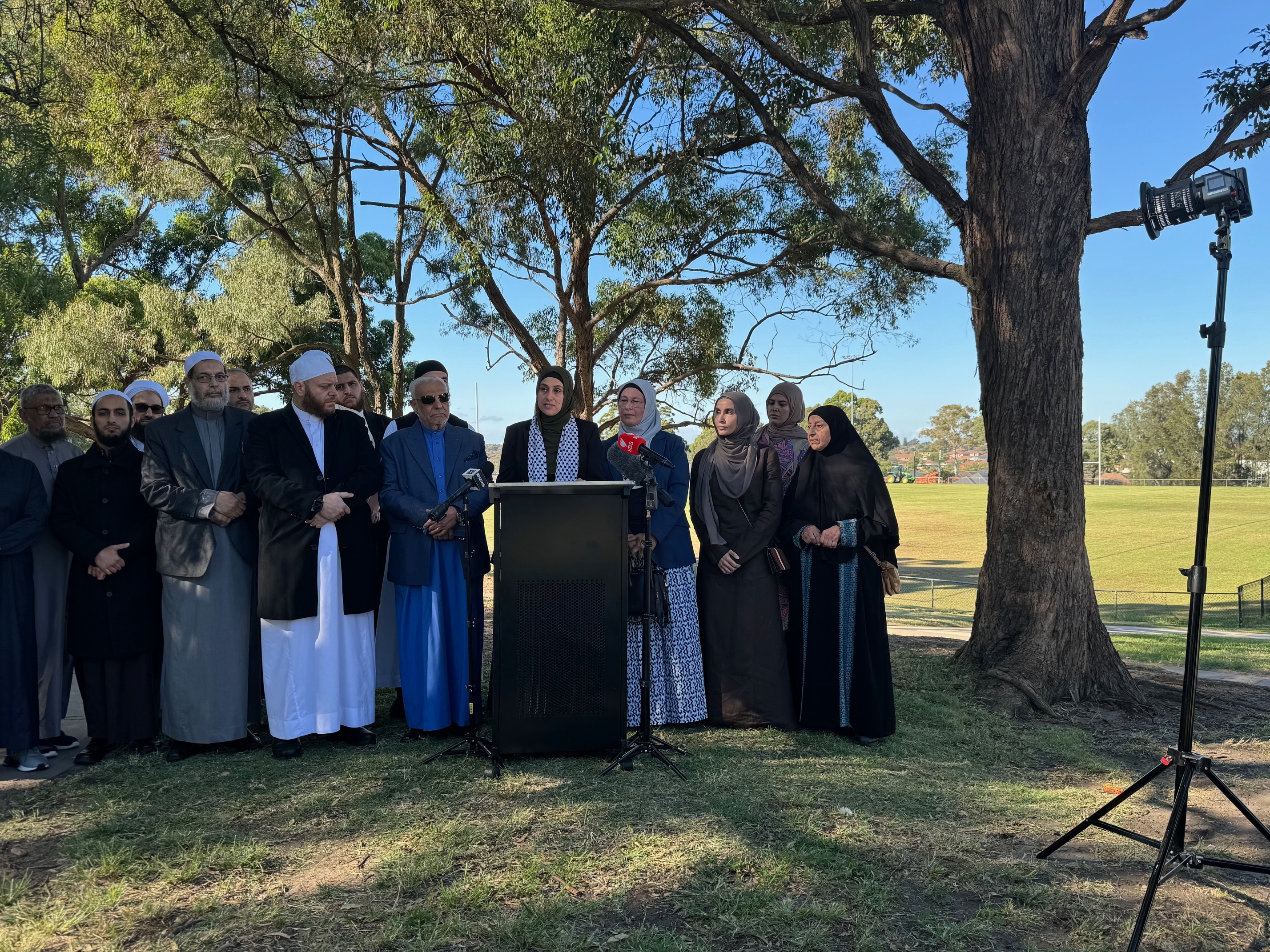 A group of Muslim leaders gather together in a line in a park