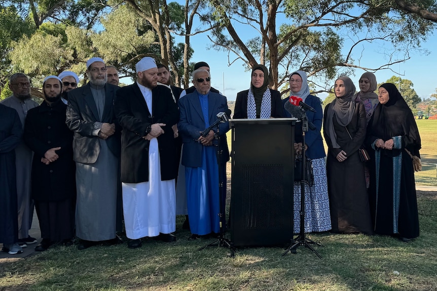 A group of Muslim leaders gather together in a line in a park