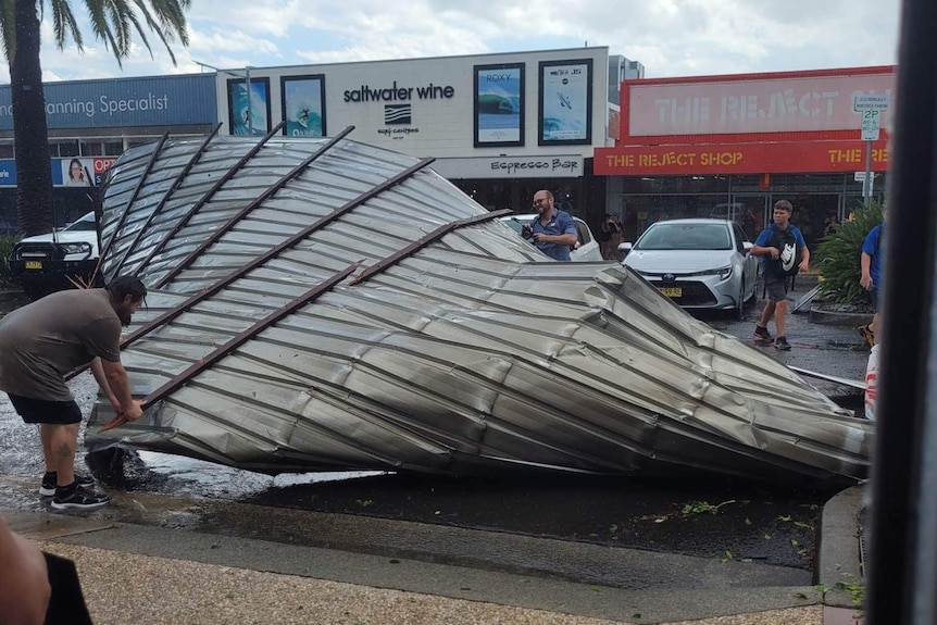 People remove a mangled iron roof from a street