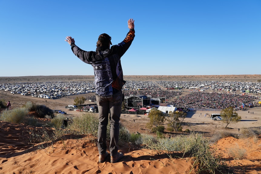 A man standing on top of a sand dune with his arms in the air.