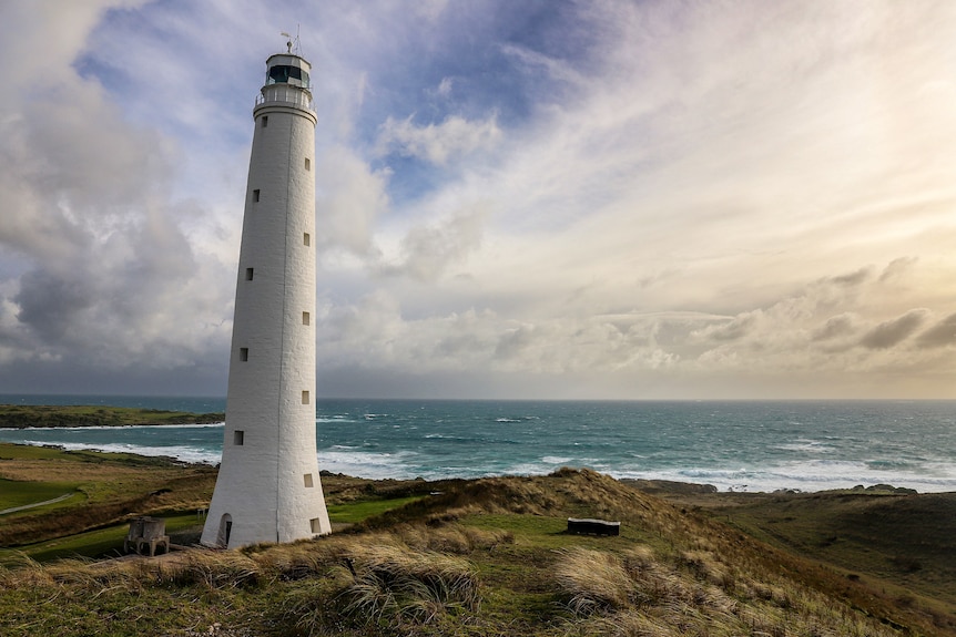 A white painted lighthouse on the coastline with blue ocean and moody skies