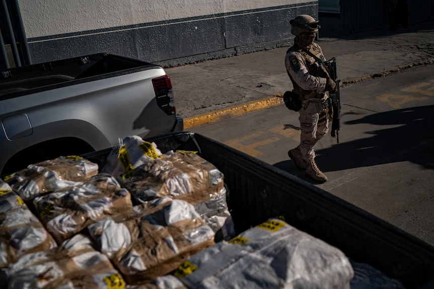 A Mexican solider holding an automatic weapon stands next to a ute with bags and bags of fentanyl