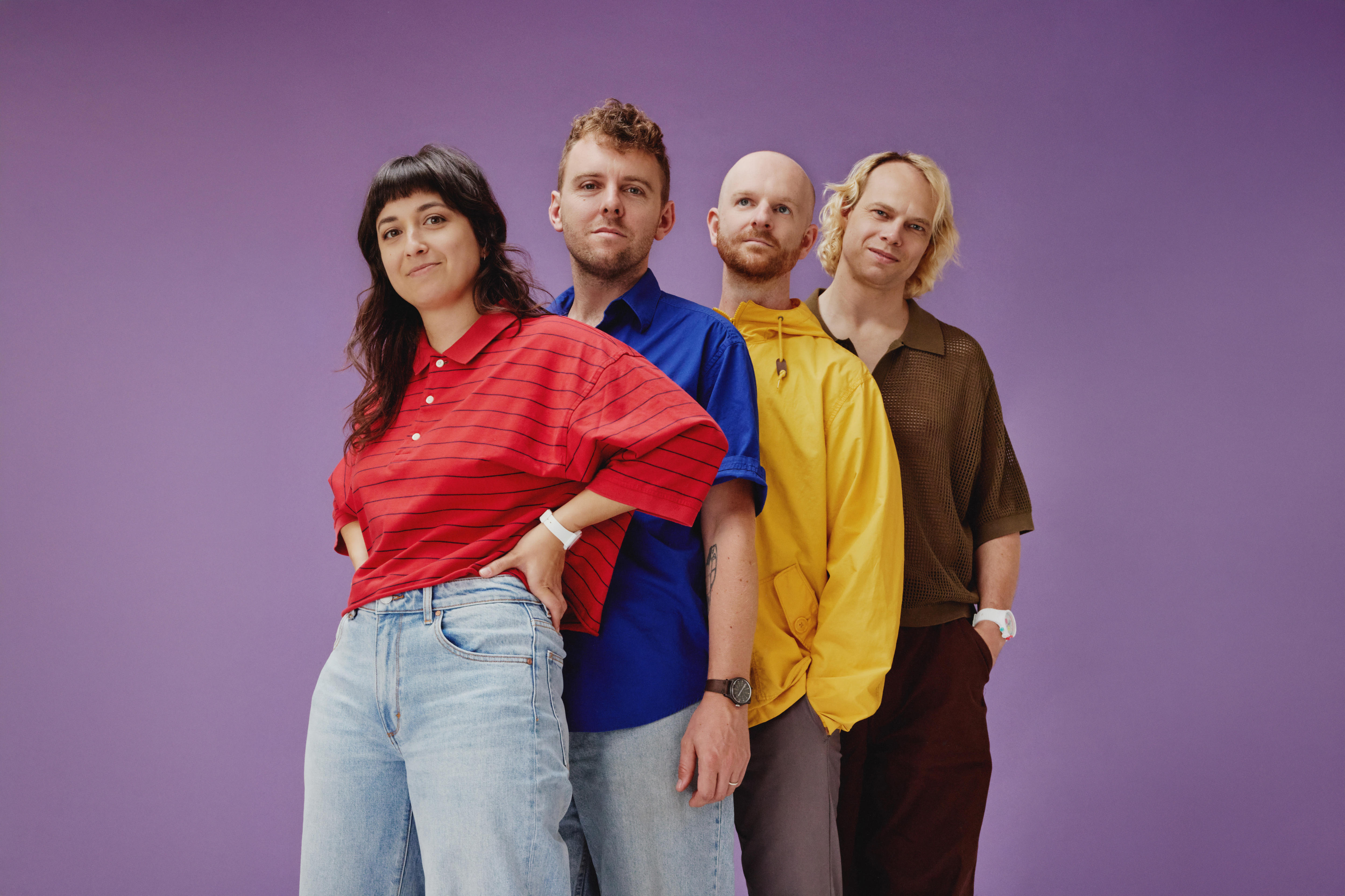 A woman and three men stand in a row before a purple background.