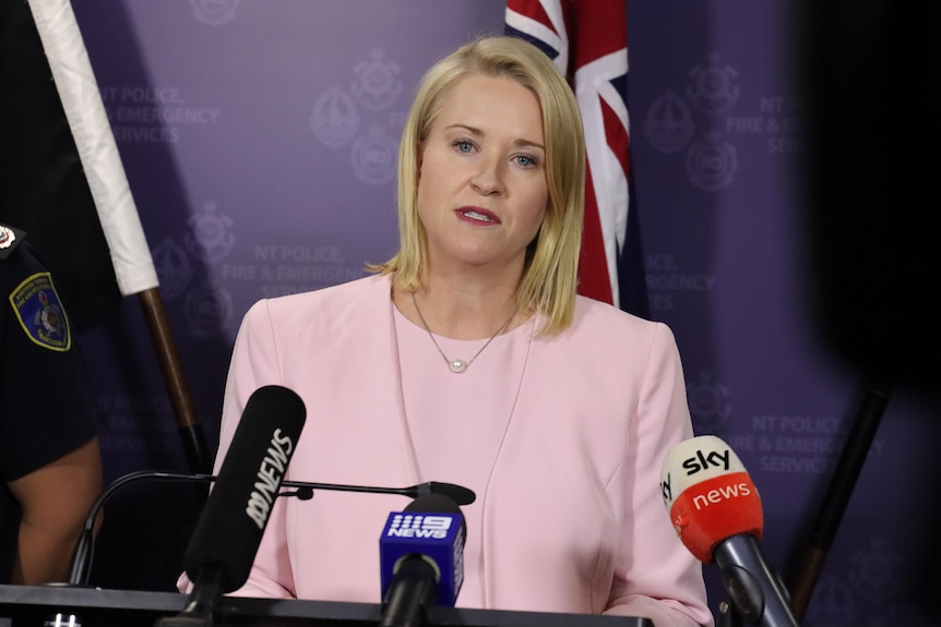 Nicole Manison stands behind a number of media microphones in front of an Australian flag