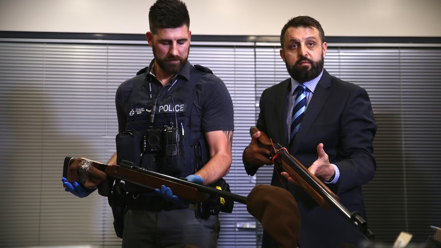 Two police officers holding old style shot guns in an office room
