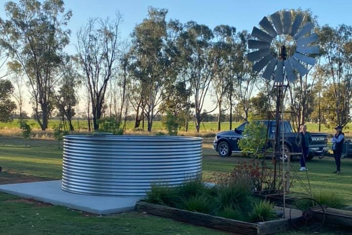 A steel tank filled with water sits on concrete slab next to windmill. 