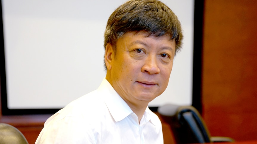 A man in a white shirt sits in a meeting room.