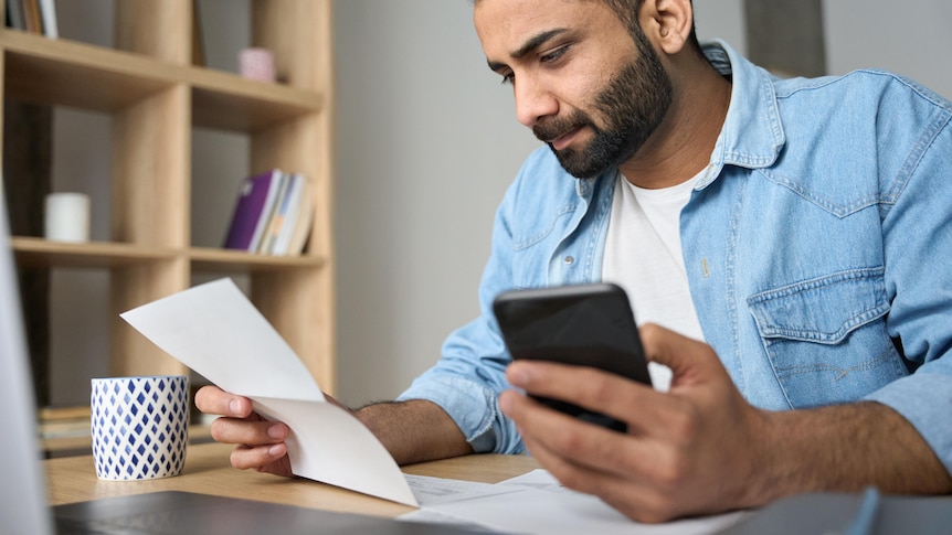 A man holds a receipt while using a laptop.