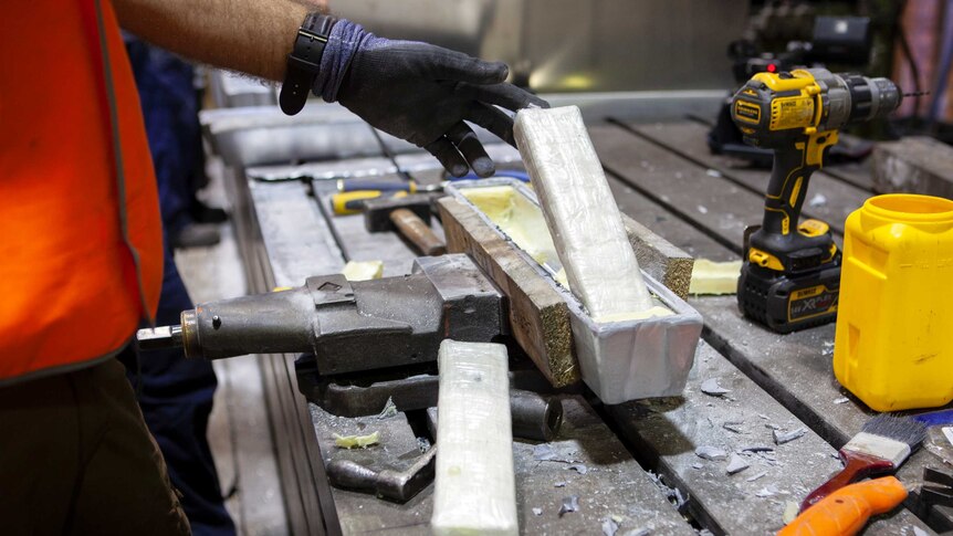 A man lifts cocaine out of an ingot on a workbench.