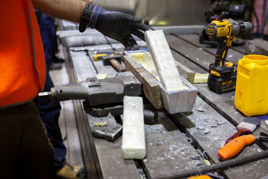 A man lifts cocaine out of an ingot on a workbench.