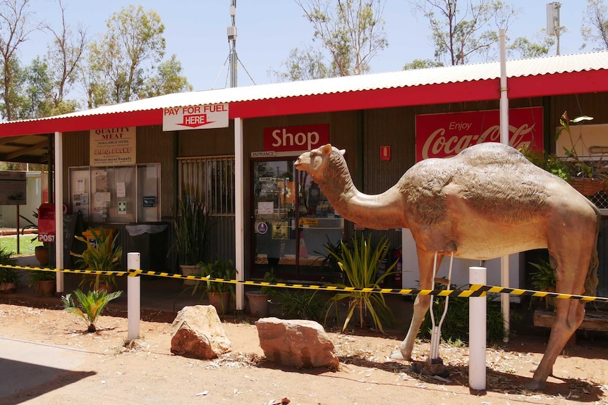 An exterior of the bar at Stuarts Well. There is a camel statue out the front and signs for a shop, meat and fuel.